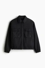 Campera negra de corte holgado, estilo cargo, con cuello camisero, cierre frontal y dos bolsillos grandes con solapa en el pecho. Posee elástico revestido en puños y bajo.
