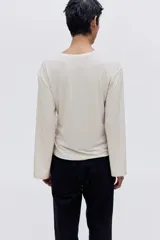 Top de manga larga confeccionado en punto suave, con diseño de hombros caídos, escote redondo y detalle de tira lateral para anudar en la cintura.