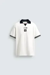 Polo de corte relajado confeccionado en piqué de algodón color blanco. Presenta cuello solapa en color negro con abertura frontal, mangas cortas con ribetes a contraste y estampado conmemorativo USA 94 FIFA World Cup.