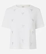 Remera de algodón color blanco, de cuello redondo y manga corta. Presenta aplicaciones de lazos en hotfix plateados distribuidos en el frente.