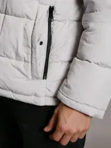 Campera puffer Calvin Klein acolchada, de color gris claro, con cuello alto, cierre frontal con cremallera negra y bolsillos laterales con cierre.