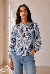 Camisa de manga larga con estampado floral en tonos azules y blancos, cuello con volados y detalles de encaje a lo largo de la botonadura y en las mangas.