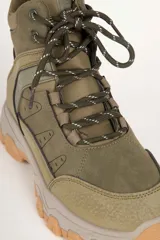 Zapatilla tipo hiking de caña media, confeccionada en una combinación de símil cuero y nylon en tonos beige y rosa suave. Presenta cordones al tono, interior acolchado para mayor abrigo y suela de goma dentada en color marrón con entresuela gris.