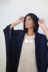 Ruana tejida en cinta con capucha integrada y terminaciones con flecos largos en los extremos.