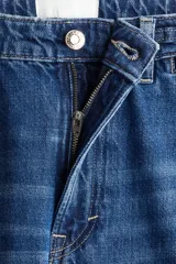 Jeans de tiro alto, pierna ancha y corte recto, confeccionado en denim de algodón rígido de color azul medio. Presenta un detalle de herrajes metálicos en la cintura.