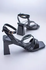 Sandalias negras de cuero sintético con tiras finas cruzadas en el empeine, pulsera al tobillo con hebilla y taco geométrico.