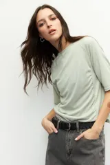 Remera negra de cuello redondo y manga tres cuartos, confeccionada en tela con textura sutil. Presenta fruncidos laterales que aportan caída y movimiento a la prenda.