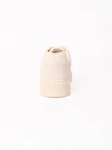 Championes de plataforma baja de color beige, con cordones tono sobre tono y detalle de placa metálica en los cordones.