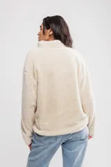 Buzo de sherpa color crema con cierre parcial con cremallera, cuello alto y bolsillos laterales.