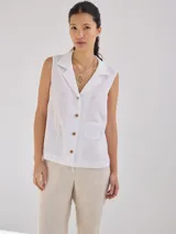 Camisa sin mangas de lino, color blanco, con cuello solapa, cierre frontal con botones y bolsillo pequeño en el pecho. Presenta costuras decorativas a la vista que definen la silueta.