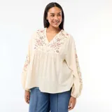 Blusa de color beige con cuello en V, mangas largas abullonadas con puños elásticos y bordados florales en el pecho y las mangas.