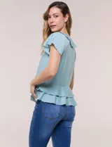 Blusa de satén texturizado color verde menta, con escote en V y volados que bordean el cuello. Presenta mangas cortas acampanadas y doble nivel de volados en la parte inferior, formando una silueta péplum.