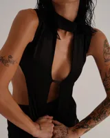 Conjunto de dos piezas compuesto por un top sin mangas con cuello alto y diseño de aberturas laterales y frontales, y una minifalda ajustada a juego. Ambas prendas están confeccionadas en tela satinada de color negro.