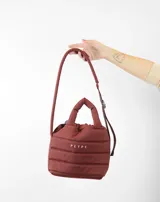 Bolsito tipo tote acolchado de color amarillo, con diseño de líneas horizontales y logo de la marca estampado en el frente. Cuenta con dos asas superiores acolchadas y una correa ajustable de cinta en color beige.