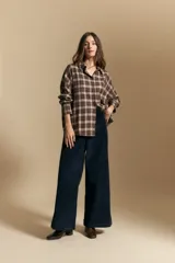 Camisa de estilo leñador con estampado de cuadros en tonos azul, negro y marrón. Presenta cuello clásico, cierre frontal con botones y mangas largas con puños abotonados.