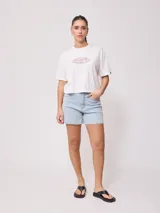 Remera blanca de algodón con calce holgado y largo cropped. Estampado frontal con el logo de la marca Rusty en óvalo con borde rosa y celeste.