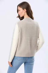 Buzo tejido de abrigo con cuello redondo y manga larga. Presenta un diseño de bloques de color en tonos gris claro y beige.