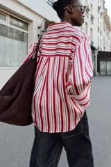 Camisa de cuello solapa con estampado de rayas verticales en tonos rojos, rosas y blancos. Presenta cierre frontal con botones y mangas tres cuartos con puño vuelto.