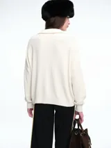 Sweater de tejido de punto color beige, con diseño de trenzas en el frente y mangas lisas. Presenta cuello polo con escote en V y puños y ruedo acanalados.