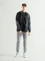 Campera deportiva negra de nylon impermeable con capucha y cierre frontal. Presenta puños y cintura elásticos de tejido acanalado. Tiene un pequeño logo blanco en el pecho.