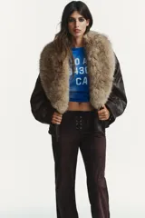 Pantalón de tiro bajo confeccionado en gamuza marrón, con diseño flare y detalle de lazada frontal. Presenta costuras marcadas y cierre lateral con cremallera.