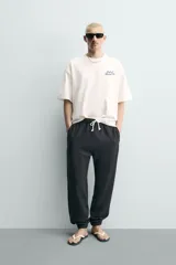 Camiseta blanca de corte relajado, con cuello redondo, manga corta y texto estampado en contraste en el pecho.