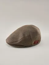 Boina estilo irlandés con diseño de espigado en tonos marrones y beige. Presenta una etiqueta decorativa lateral en color rojo.