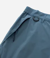 Pantalón de corte holgado en color azul petróleo, confeccionado en microfibra de poliéster. Presenta un diseño utilitario con múltiples bolsillos funcionales, cierres visibles y detalles técnicos en las piernas.