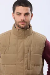 Chaleco reversible acolchado con diseño capitoneado. Un lado presenta un acabado en color beige con cierre frontal y bolsillo vertical en el pecho, mientras que el otro lado es de color azul marino. Cuenta con cuello alto y relleno térmico para mayor abrigo.