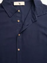 Camisa blanca de manga larga con corte regular en tejido lino-viscosa, ideal para los días de verano. Tiene botones de madera y parche con logo de la marca.