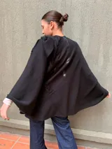 Capa negra de tejido de punto en lana con apliques de cuero y cuello drapeado.