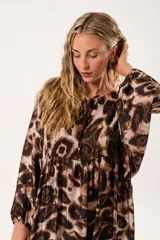 Vestido midi de corte holgado con estampado animal print en tonos marrones y beige. Tiene cuello redondo con lazo, mangas largas abullonadas y falda amplia con volantes. Incluye cinturón marrón con tachas.