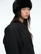 Blazer de corte sastrero con diseño de doble botonadura y solapas clásicas. Presenta un patrón de rayas verticales finas, hombros estructurados y bolsillos con solapa en la parte frontal.