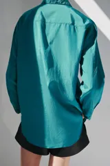 Camisa de corte fluido con cuello solapa y manga larga. Presenta cierre frontal con botones y dos bolsillos de plastrón con solapa en el pecho. El diseño cuenta con bajo redondeado y costuras verticales decorativas.