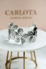 Pulsera rígida plateada con diseño de flores texturizadas.