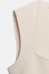 Body de tejido elástico color beige, sin mangas y con diseño de escote cuadrado. Cuenta con cierre en la parte inferior con botones a presión.