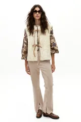 Chaleco reversible de gamulán de oveja en color natural, con corte holgado, cuello a la base y terminaciones al corte. Presenta tiras de cuero en el frente para atar.