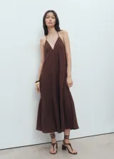 Vestido midi de algodón con textura, diseño evasé y corte holgado. Presenta escote en pico, tirantes finos que se atan al cuello y detalles fruncidos en la falda.