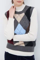 Chaleco de punto con diseño de rombos en tonos beige, marrón y gris. Presenta cuello redondo y corte ajustado a la cintura.