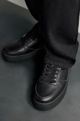 Zapatillas deportivas de estilo retro, color negro, con diseño superior de paneles combinados, cordones al tono y suela gruesa con volumen.