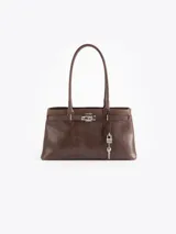 Cartera tipo shopper de cuero vacuno marrón, con silueta estructurada, doble asa de hombro y herrajes metálicos plateados. Incluye tira decorativa con candado y llave colgantes.