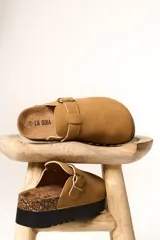 Zueco de plataforma color camel, confeccionado en material tipo gamuza, con detalle de hebilla metálica lateral y base de corcho con suela de goma negra.