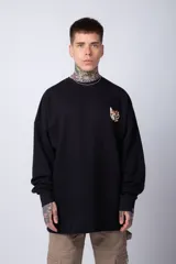 Buzo de tejido friza color crema, de corte oversize y cuello redondo. Presenta un pequeño bordado o parche en el pecho izquierdo con un diseño de cabeza de animal en tonos rojizos/terracota.