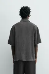 Camisa de corte relajado con textura de rayas verticales, cuello solapa y manga corta. Presenta cierre frontal con botones a tono.