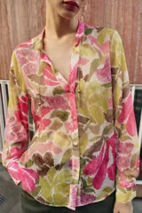 Blusa de manga larga con estampado floral en tonos rosados, verdes y beige. Presenta escote en pico con detalle de abalorios colgantes y cierre frontal con botones.