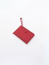 Billetera roja de diseño compacto con cierre superior y bolsillo frontal con botón a presión. Incluye una correa de mano lateral.