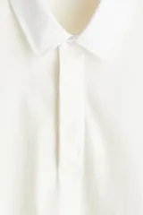 Remera polo de manga larga confeccionada en punto suave de algodón, con cuello inglés de sarga y tapeta con botones ocultos. Presenta hombros caídos, puños acanalados y aberturas laterales en el bajo, con un corte holgado.