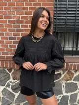 Camisa blanca de manga larga con detalles de encaje o bordado en el canesú y el frente. Presenta un corte holgado y mangas con puños elásticos o fruncidos.