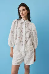 Camisa de broderie color blanco, con cuello clásico, mangas abullonadas y cierre frontal oculto.