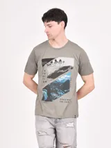 Remera de manga corta color gris jaspeado con cuello redondo. Estampado frontal con diseño de paisaje dividido en dos secciones: una con palmeras y otra con montañas nevadas, con texto que incluye "Expedition", "Summer Times", "Chill Out" y "Chasing The Sun".